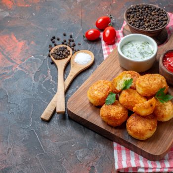 bottom-view-chicken-nuggets-wood-board-with-sauces-cherry-tomatoes-wooden-spoons-black-pepper-bowl-dark-table (1)